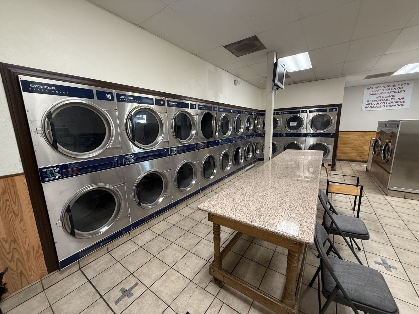 Rows of stacked dryers and a folding table inside EZ Stop Laundromat